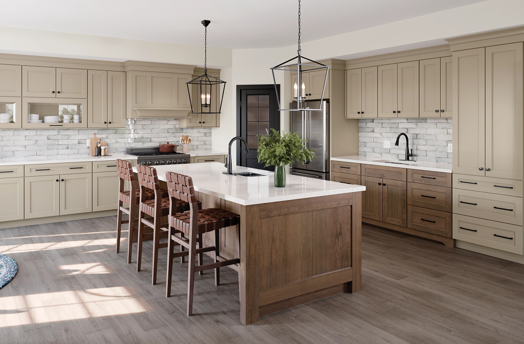 Greige shaker kitchen with a limewashed brick backsplash, a mantel-style hood and matte black hardware, centred on a mid-brown wood-toned island